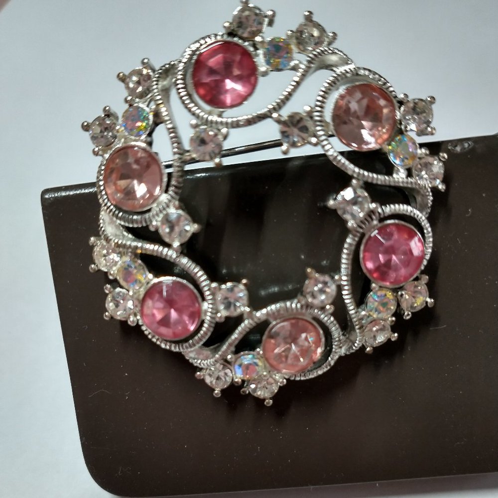 Silver round brooch with pink inserts.